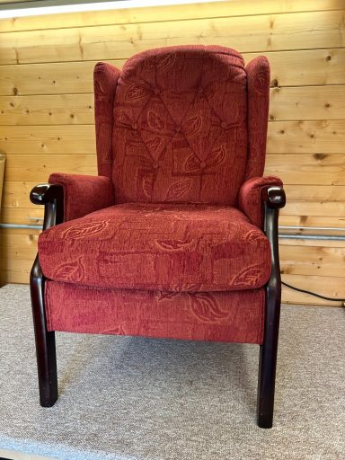 Red patterned armchair with dark wooden arms and legs, set against a wooden backdrop.